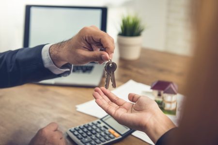 Real estate broker agent giving house keys to client after finish making rental agreement in the office
